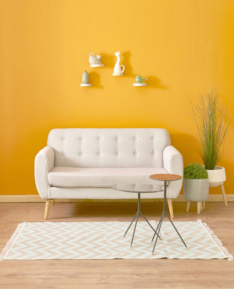Gelbe Wand mit weißem Sofa, Tisch, Teppich und Pflanzen
