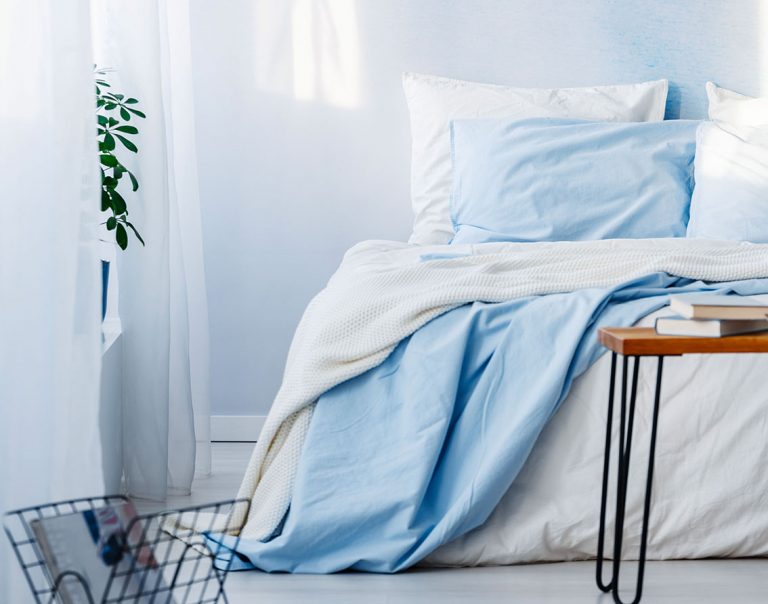 Teil eines Bettes vor einer hellblauen Wand mit weißer und hellblauer Bettwäsche