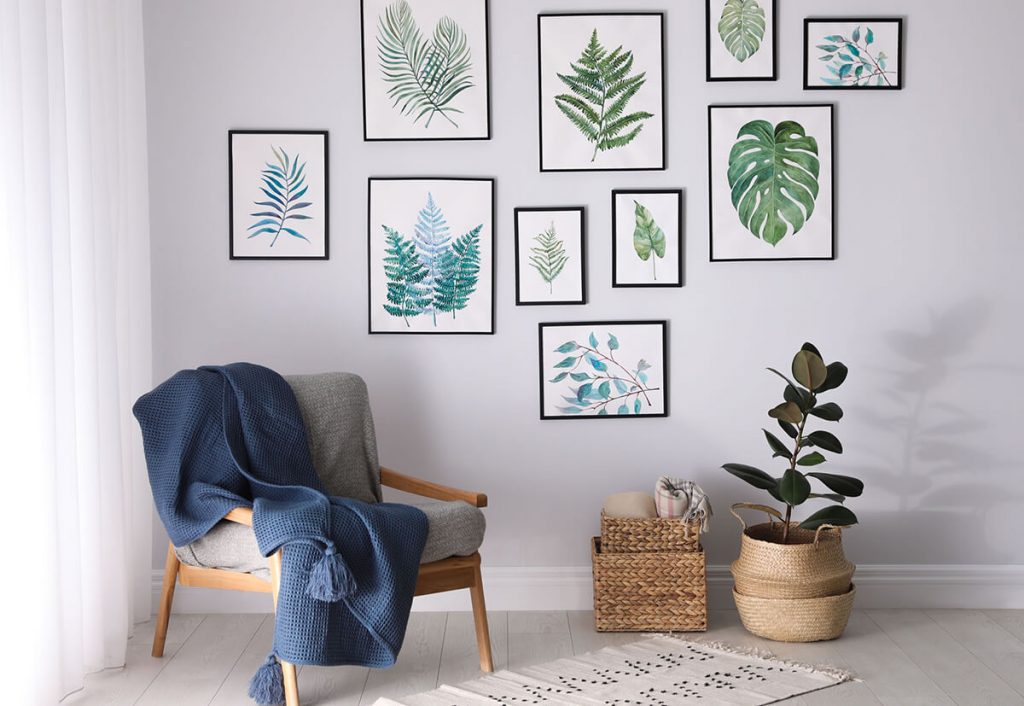 Bilderrahmen mit Blättermotiven an hellgrauer Wand, davor Sessel mit dunkelblauer Decke