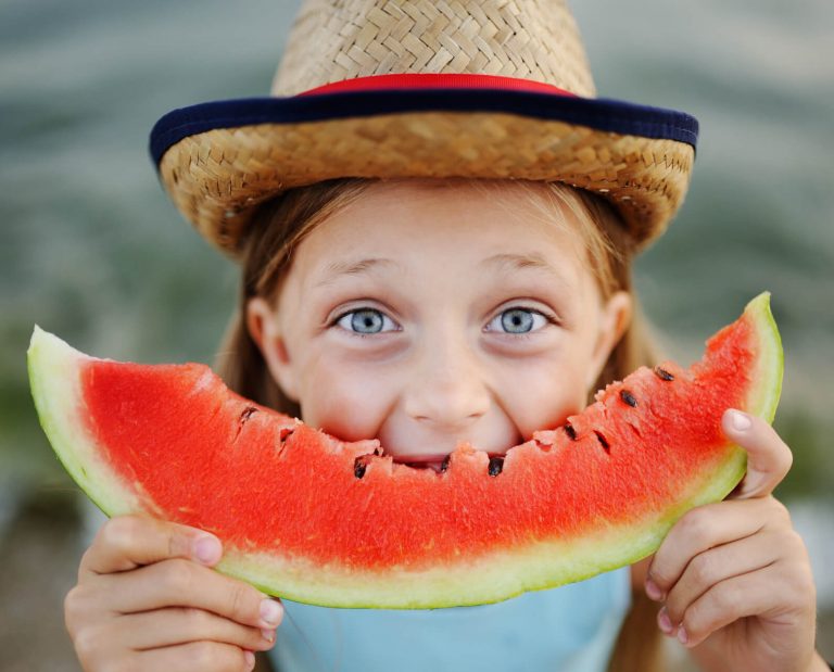 Kind hält Melonenschnitz vor den Mund