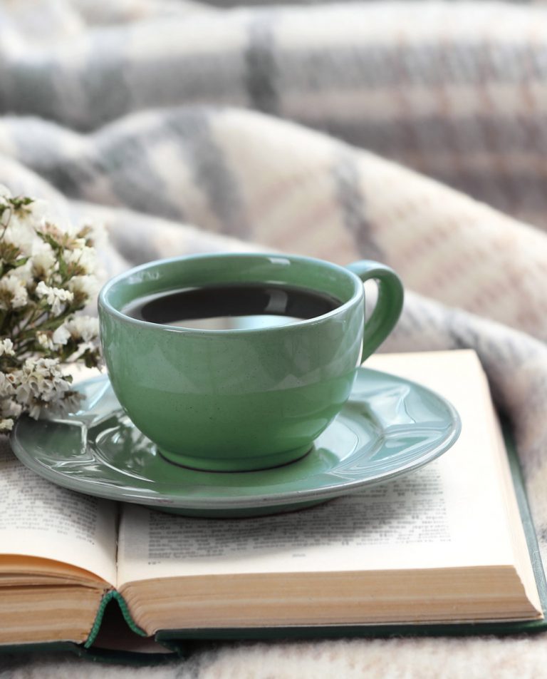 grüne Tasse mit Tee stehend auf einem aufgeschlagenen Buch