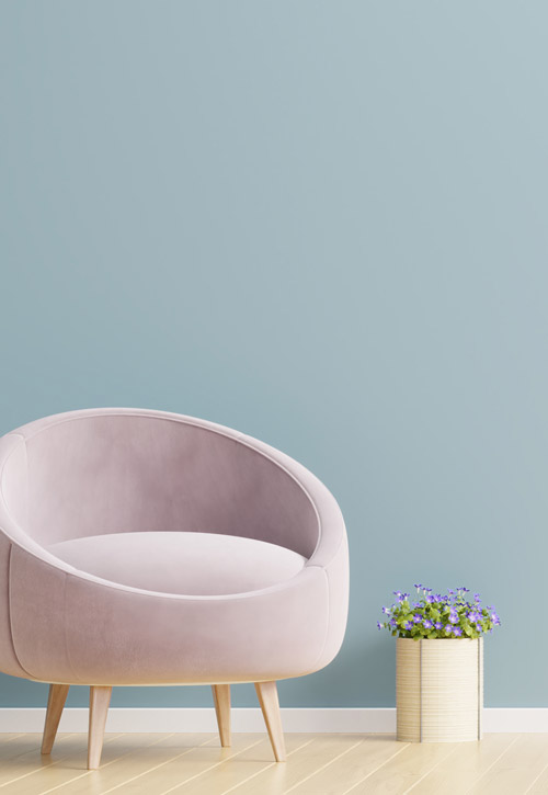 moderner Sessel in rosanem Samtbezug vor blauer Wand