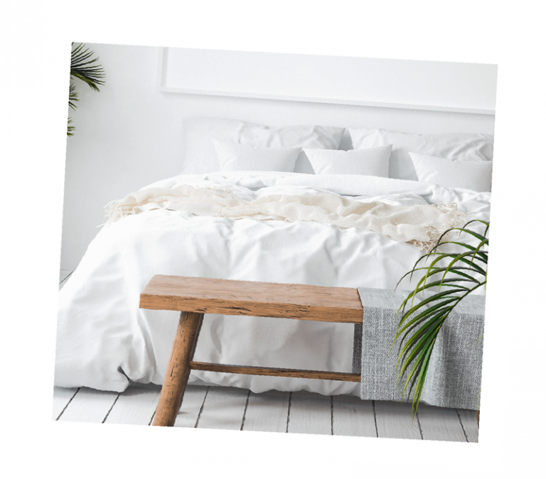 Bett mit weißer Bettwäsche und Holzbank