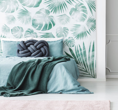 Fototapete mit Blättern, davor ein Bett mit grüner Decke