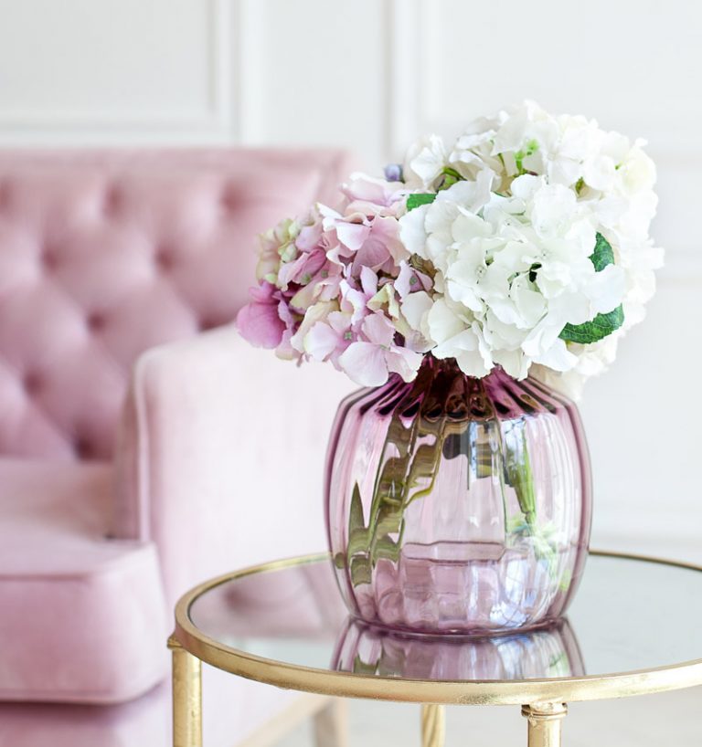 Blumen in rosaner Glasvase auf Beistelltisch