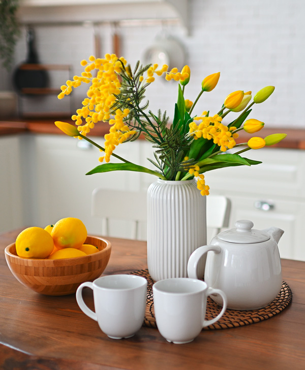 gelbe Frühlingsblumen, Zitronen und weißes Geschirr