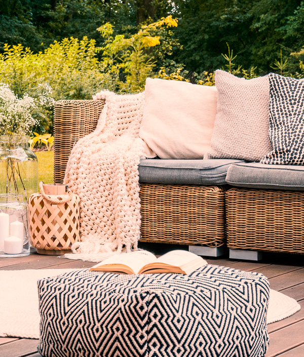 Terrasse mit Sofa aus Rattan mit Pouf und dekorativen Textilien